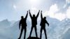 Three people stand on a mountain and raise their arms in the air