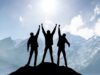 Three people stand on a mountain and raise their arms in the air